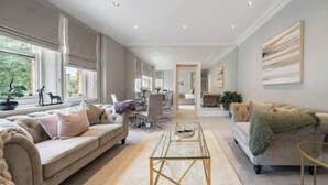 A spacious living room with a sofa, a coffee table, and a dining area in the background. - Hans Place Residences (London)