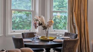 A dining table with chairs, a vase with flowers, and a window with curtains. - Hans Place Residences (London)