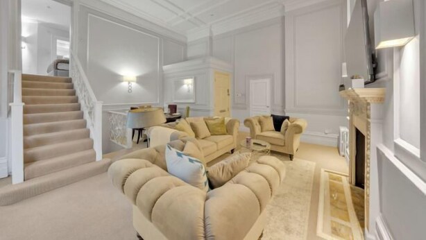 A spacious living room with a beige sofa, a fireplace, a staircase, and a dining area. - Hans Place Residences (London)