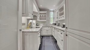 A narrow kitchen with white cabinetry, a marble countertop, and a tiled floor. - Hans Place Residences (London)