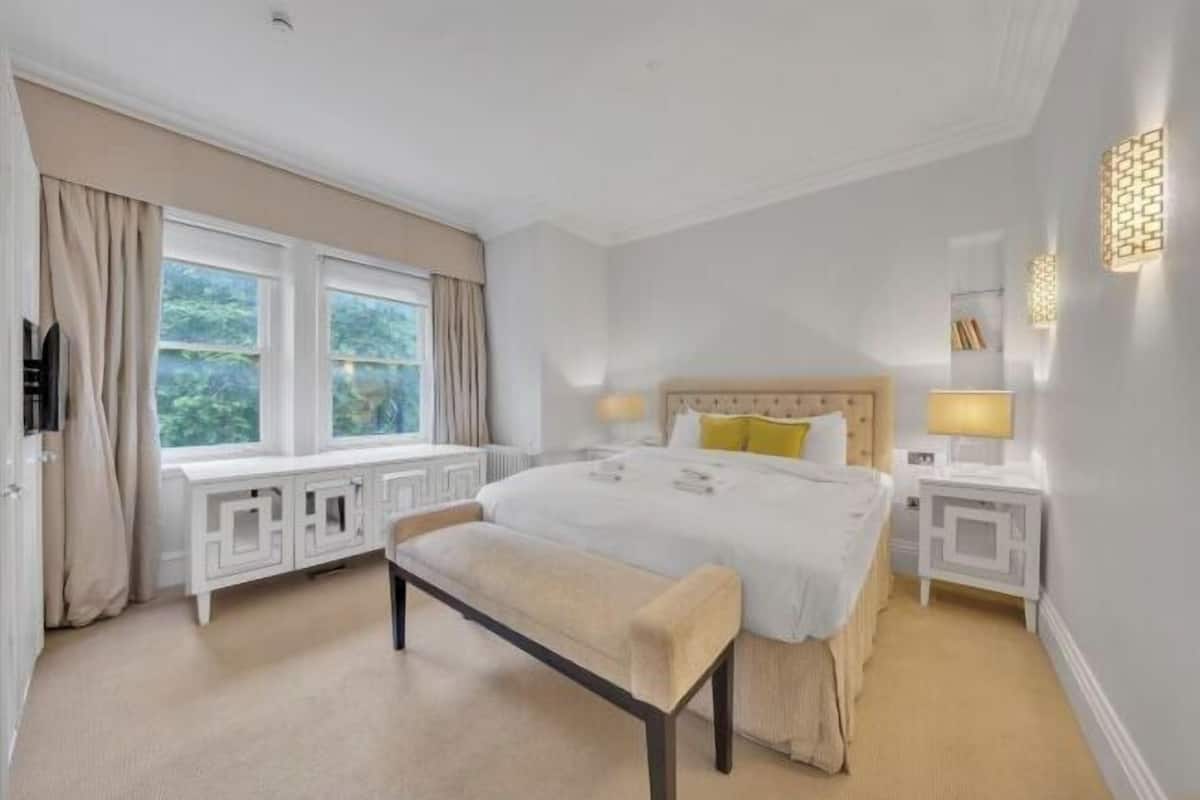 Ein Schlafzimmer mit einem großen Bett, einer Bank, zwei Nachttischen und einem Fenster mit Vorhängen.
