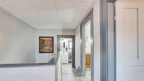 Un pasillo con piso de tonos claros, una pared blanca con un cuadro enmarcado y una puerta que da a otra habitación.