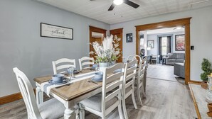 Un comedor con una mesa de madera dispuesta para seis personas, sillas blancas y un ventilador de techo.