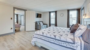 Un dormitorio con una cama grande, un televisor montado en la pared y una ventana con cortinas.