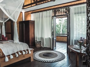 Ein Schlafzimmer mit einem hölzernen Bett, einem Holzschrank, einem gewebten Korb, einem runden Teppich und einem Balkon mit Tisch und Blumenvase.
