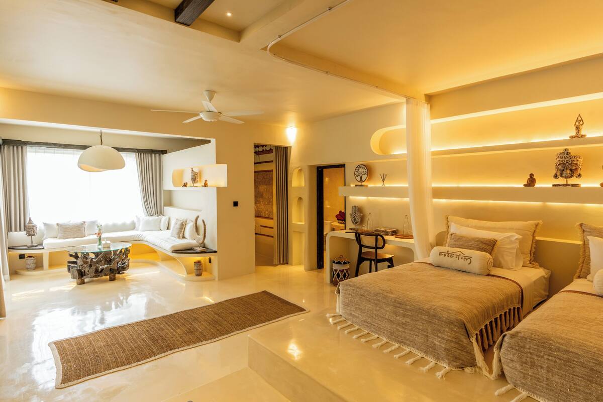 A modern hotel room with a large bed, a sofa, a desk, and a ceiling fan.