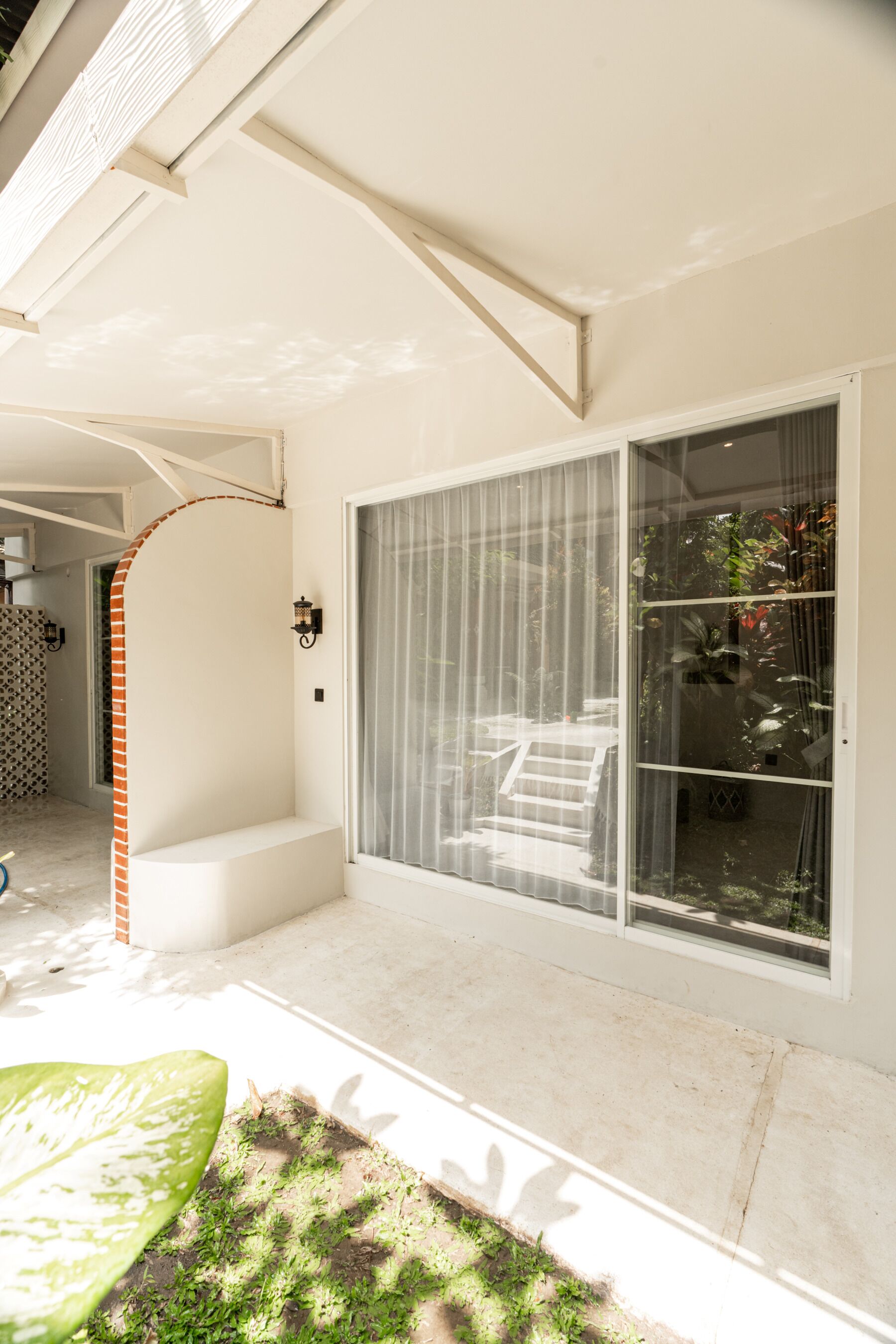 A covered outdoor area with a bench, a sliding glass door, and a small garden area.