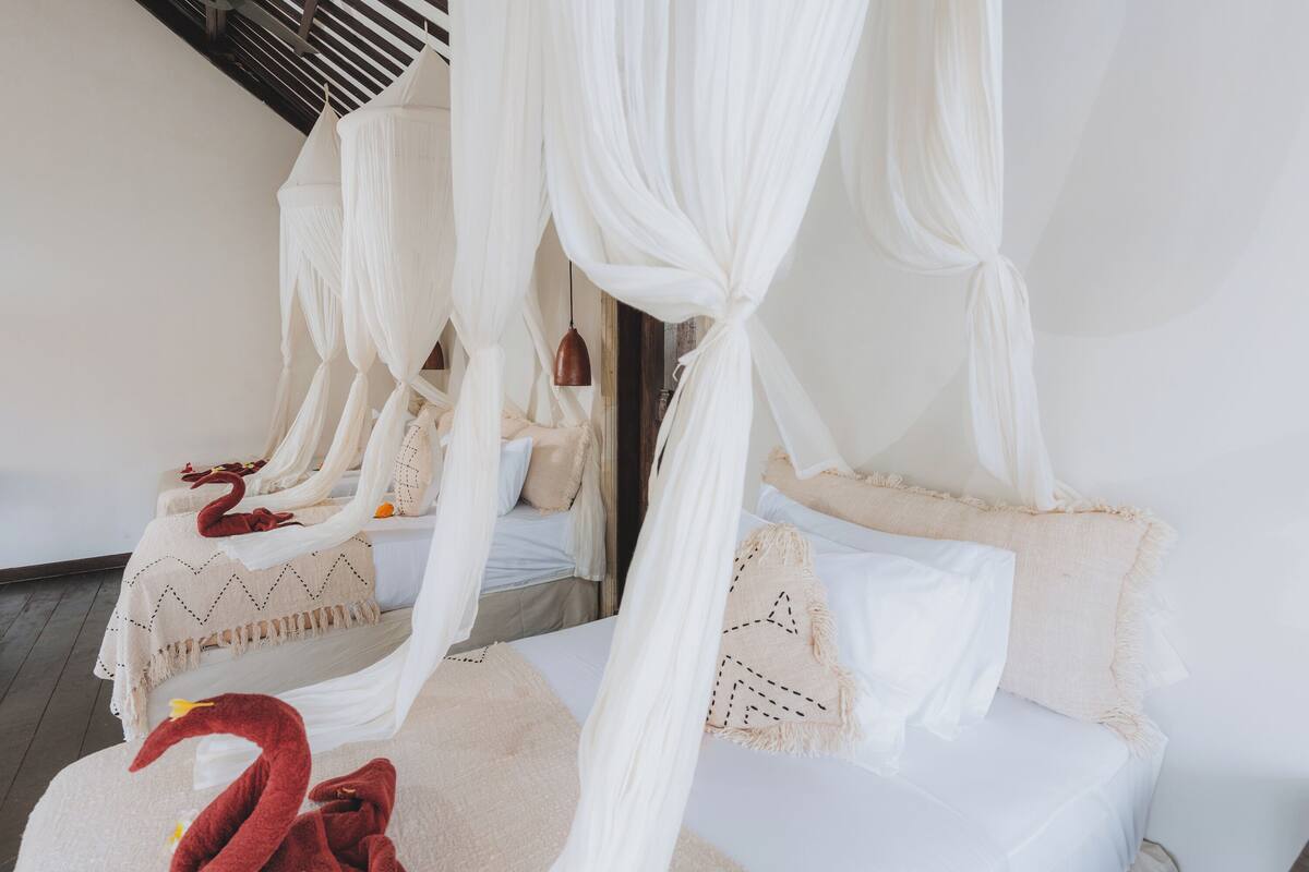 A room with two beds, each with white bedding and a canopy.