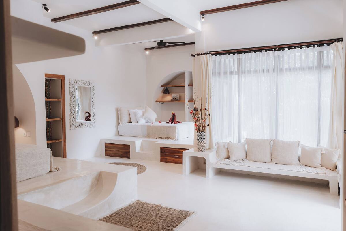 A modern living room with a sofa, a coffee table, and a fireplace. There are wooden shelves and a mirror on the wall.