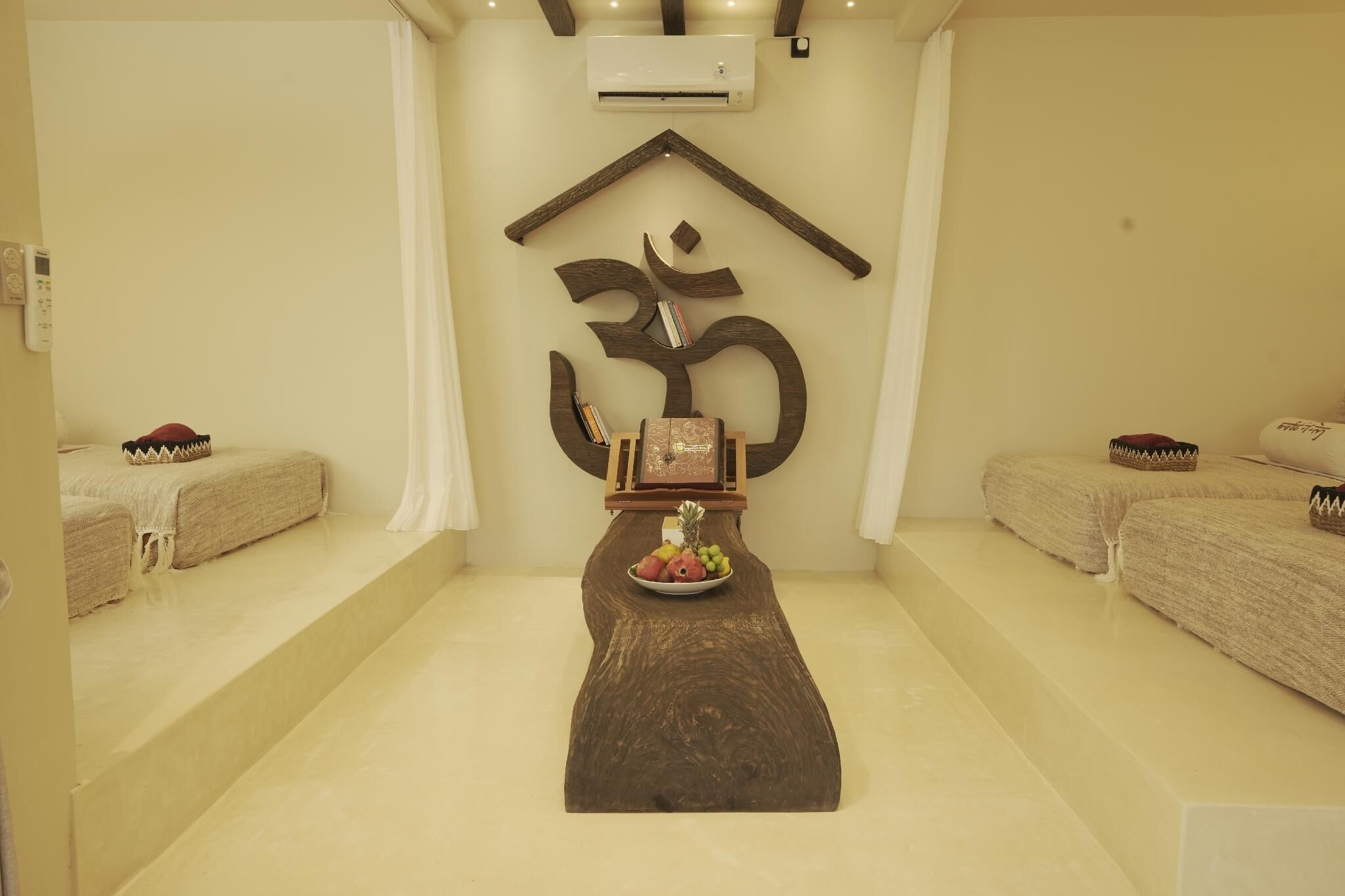 A room with a wooden table, two beds, a wall-mounted air conditioner, and a decorative symbol on the wall.
