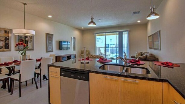 A modern kitchen with a central island, dining area with chairs, and a living space with a sofa and TV. - Serenity 3 Bedroom Vacation Home 1523 (Clermont)