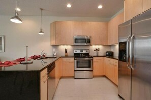 A modern kitchen with wooden cabinets, stainless steel appliances, and pendant lighting. - Serenity 3 Bedroom Vacation Home 1523 (Clermont)