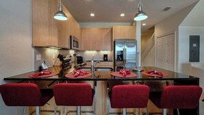 A modern kitchen with wooden cabinets, stainless steel appliances, and red bar stools. - Serenity 3 Bedroom Vacation Home 1523 (Clermont)