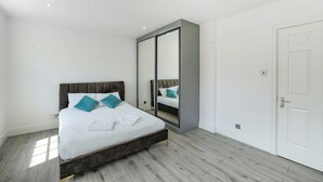 Un dormitorio moderno con una cama grande, un armario con espejo y una puerta blanca.