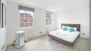 Un dormitorio con cama, dos ventanas, un radiador y un calentador portátil.