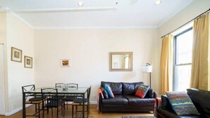 Un salon avec un canapé en cuir noir, une table à manger en verre avec des chaises, une table basse en bois et une grande fenêtre avec des rideaux.