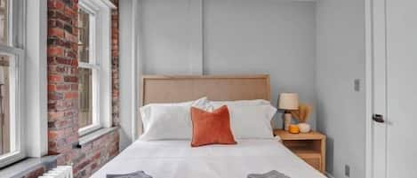 A hotel room with a bed, a nightstand, a lamp, and a window with a view of a brick wall.