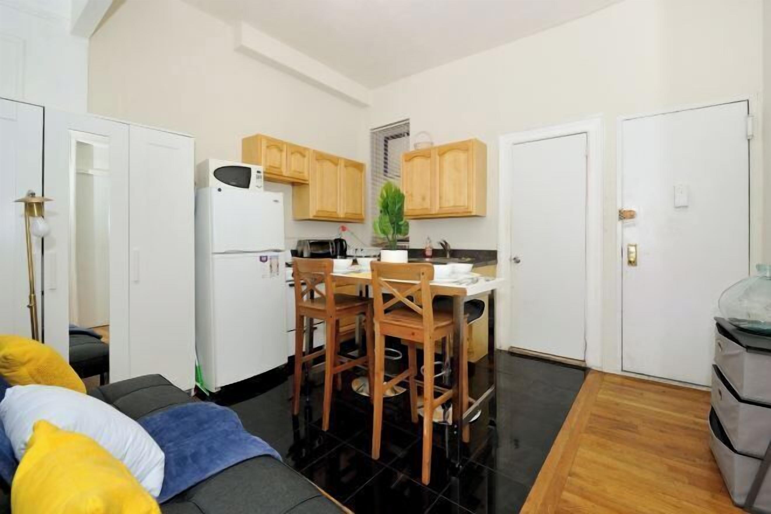 A compact kitchen with wooden cabinets, a refrigerator, and a dining table with chairs.