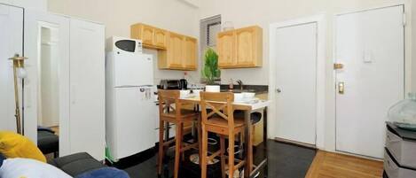 A compact kitchen with wooden cabinets, a refrigerator, and a dining table with chairs.