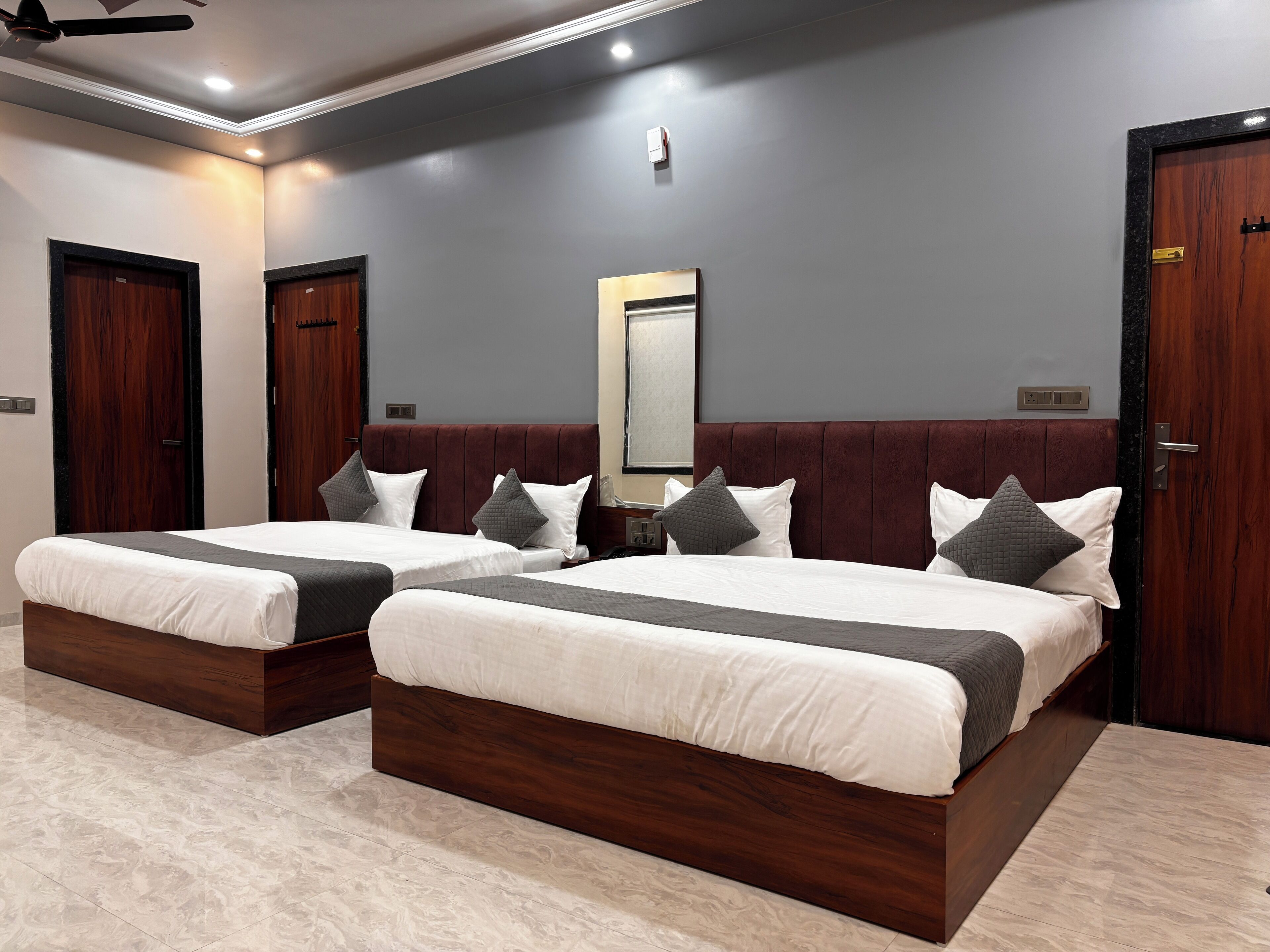 Ein Hotelzimmer mit zwei Betten, Holz-Kopfteilen, einem großen Spiegel und einem Deckenventilator.