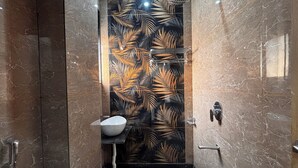A bathroom with a black and gold leaf-patterned wall, a white sink, and a shower area. - Hotel Lakshya Raj Palace - Khatushyamji (Khatoo)