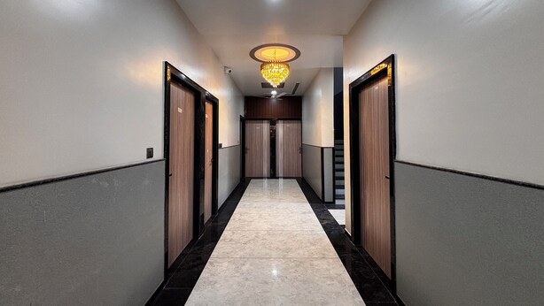 A hallway with a marble floor, wooden doors, and a chandelier. - Hotel Lakshya Raj Palace - Khatushyamji (Khatoo)