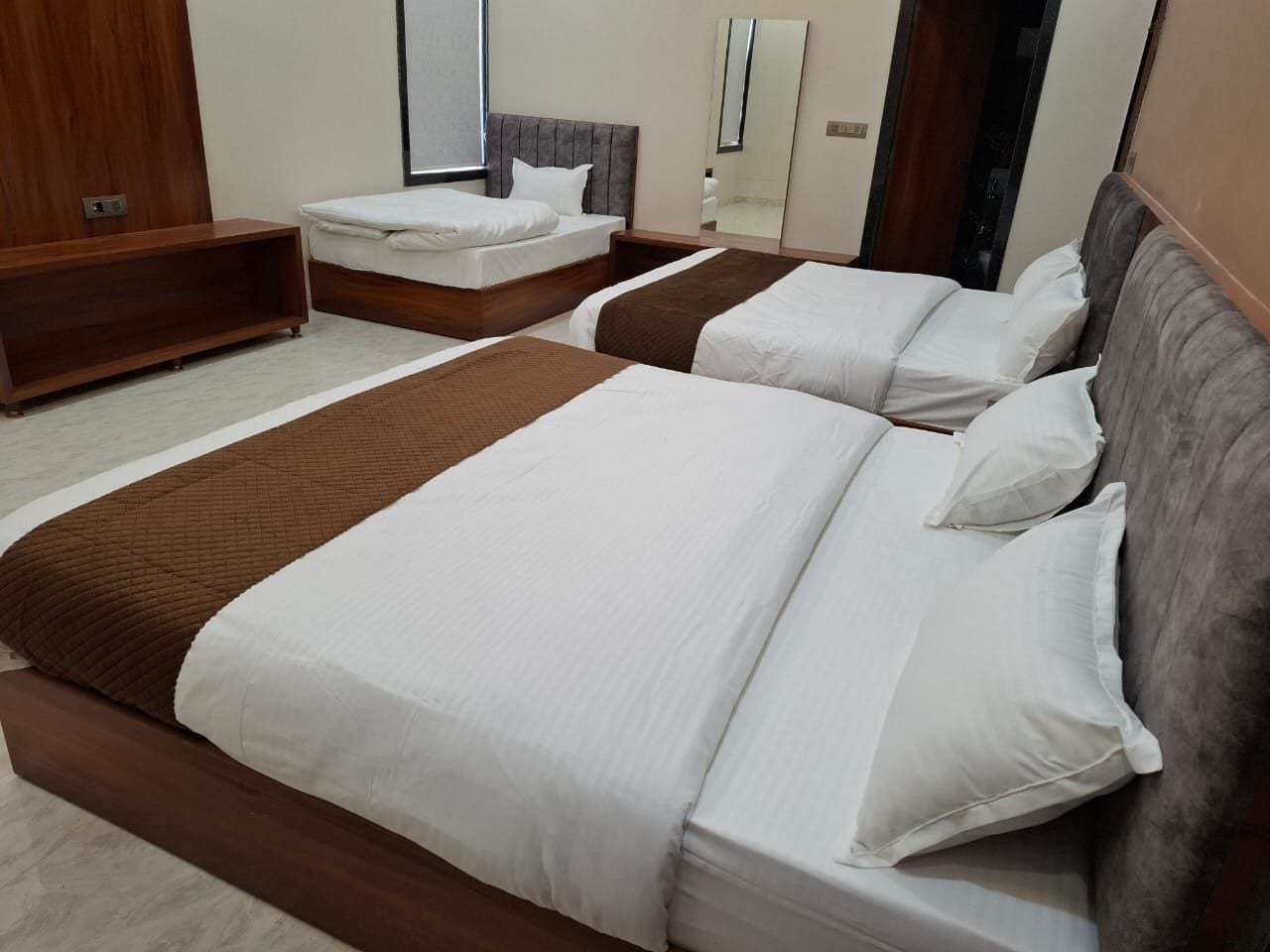 Habitación de hotel con dos camas, cabecero de madera, mesita de noche y un espejo grande.