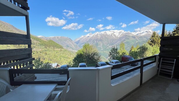 Un balcon offrant une vue sur des montagnes enneigées, avec une table, des chaises et une balustrade.