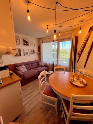 A cozy living room with a sofa, a dining table with candles, and a kitchen area. - Charming 4-person studio - Auris en Oisant domaine Alpes d'Huez (Auris)