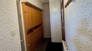 Un couloir étroit avec une armoire en bois, une armoire blanche, un radiateur et un luminaire au plafond de forme géométrique.