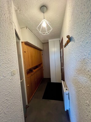 A narrow hallway with a wooden cabinet, a white wardrobe, a radiator, and a geometric ceiling light fixture. - Charming 4-person studio - Auris en Oisant domaine Alpes d'Huez (Auris)