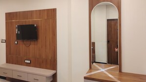 Ein modernes Zimmer mit einer Wandpaneelaus Holz, einem flachbildfernseher über einem Schminktisch und einem großen Spiegel, der eine Tür reflektiert.