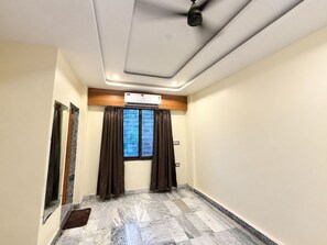 A hotel room with a marble floor, a ceiling fan, an air conditioning unit, and a window with curtains. - Shree Ji Darbar (Udaipur)