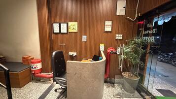 Zona de recepción de un hotel con pared de madera, mostrador de recepción, una silla y una planta en maceta.