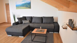A modern living room with a sectional sofa, a small wooden coffee table, and a painting on the wall. - Wanderlust apartment with 2 bedrooms, kitchen, shower/WC and loggia (Rosenheim)