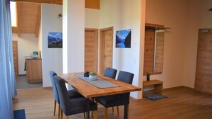 A dining area with a wooden table, black chairs, and a small plant. There are wooden doors and a view of mountains in the background. - Wanderlust apartment with 2 bedrooms, kitchen, shower/WC and loggia (Rosenheim)