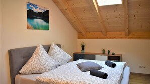 A bedroom with a bed, pillows, a nightstand, a plant, and a painting on the wall. - Wanderlust apartment with 2 bedrooms, kitchen, shower/WC and loggia (Rosenheim)