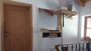Una habitación con una puerta de madera, un armario blanco con cajones, una estantería con cestas y una ventana con vistas.