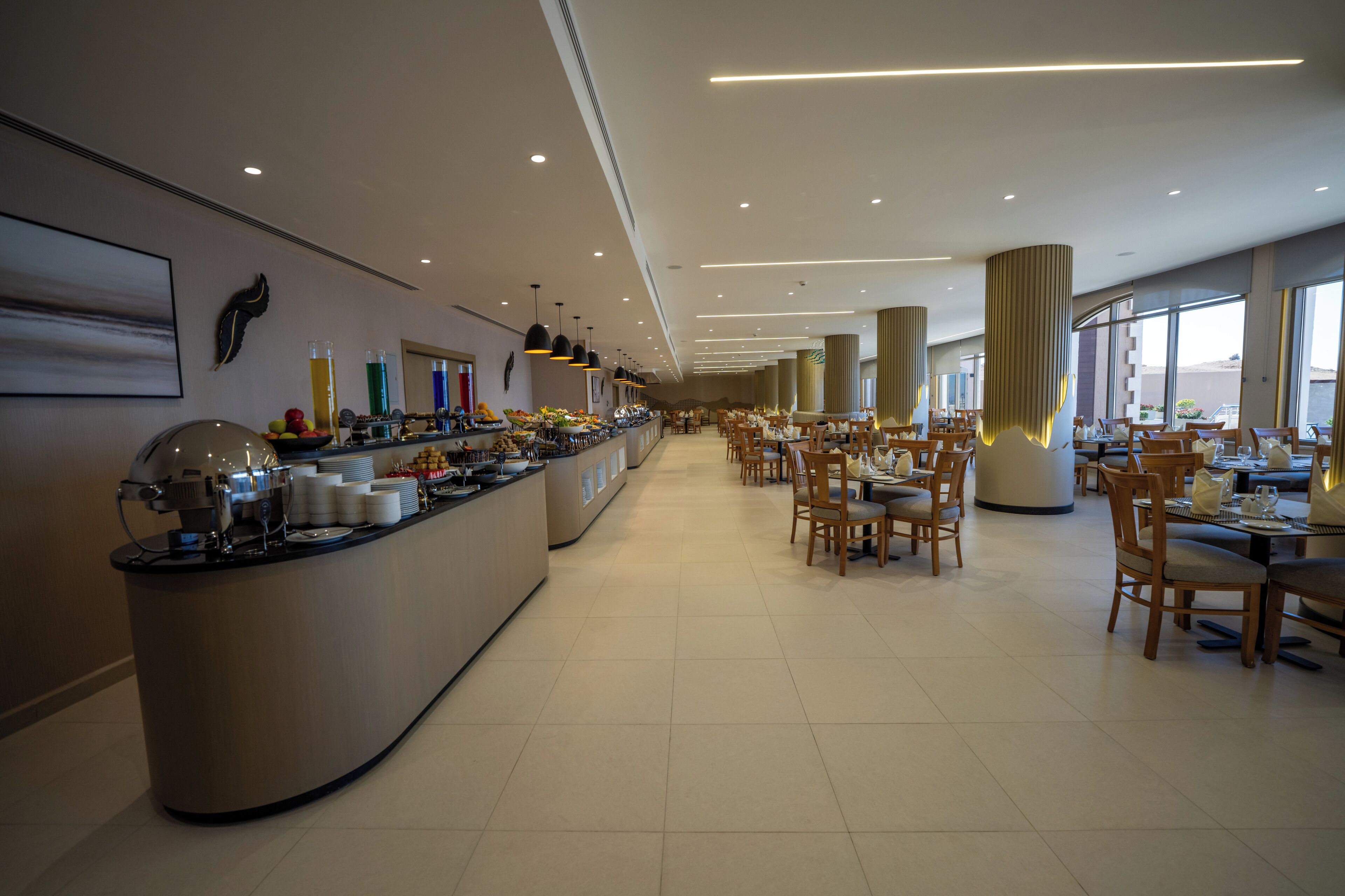 A spacious hotel dining area with a buffet counter, multiple dining tables, and chairs.
