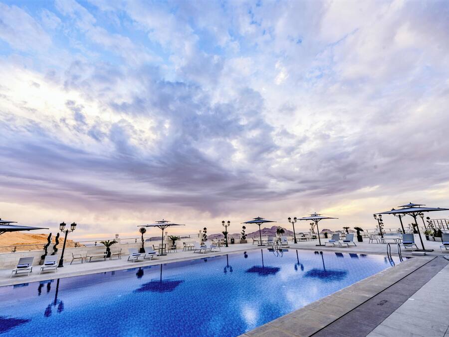 A swimming pool with lounge chairs and umbrellas, surrounded by a desert landscape.
