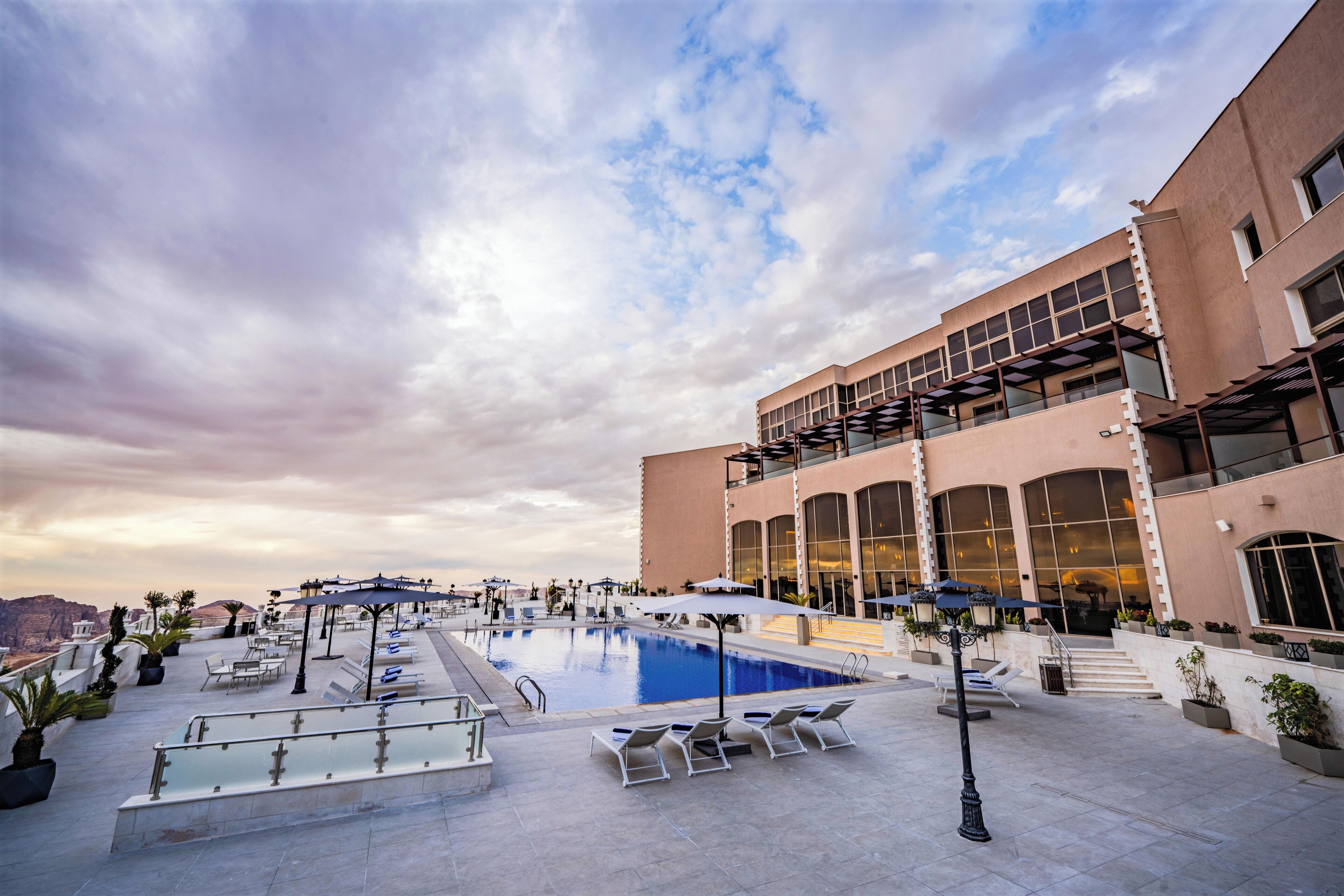 A rooftop pool area with lounge chairs, umbrellas, and a building with large windows and a modern design.