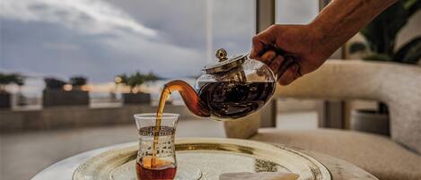 A hand pouring tea into a glass on a tray with a view of the sea in the background.