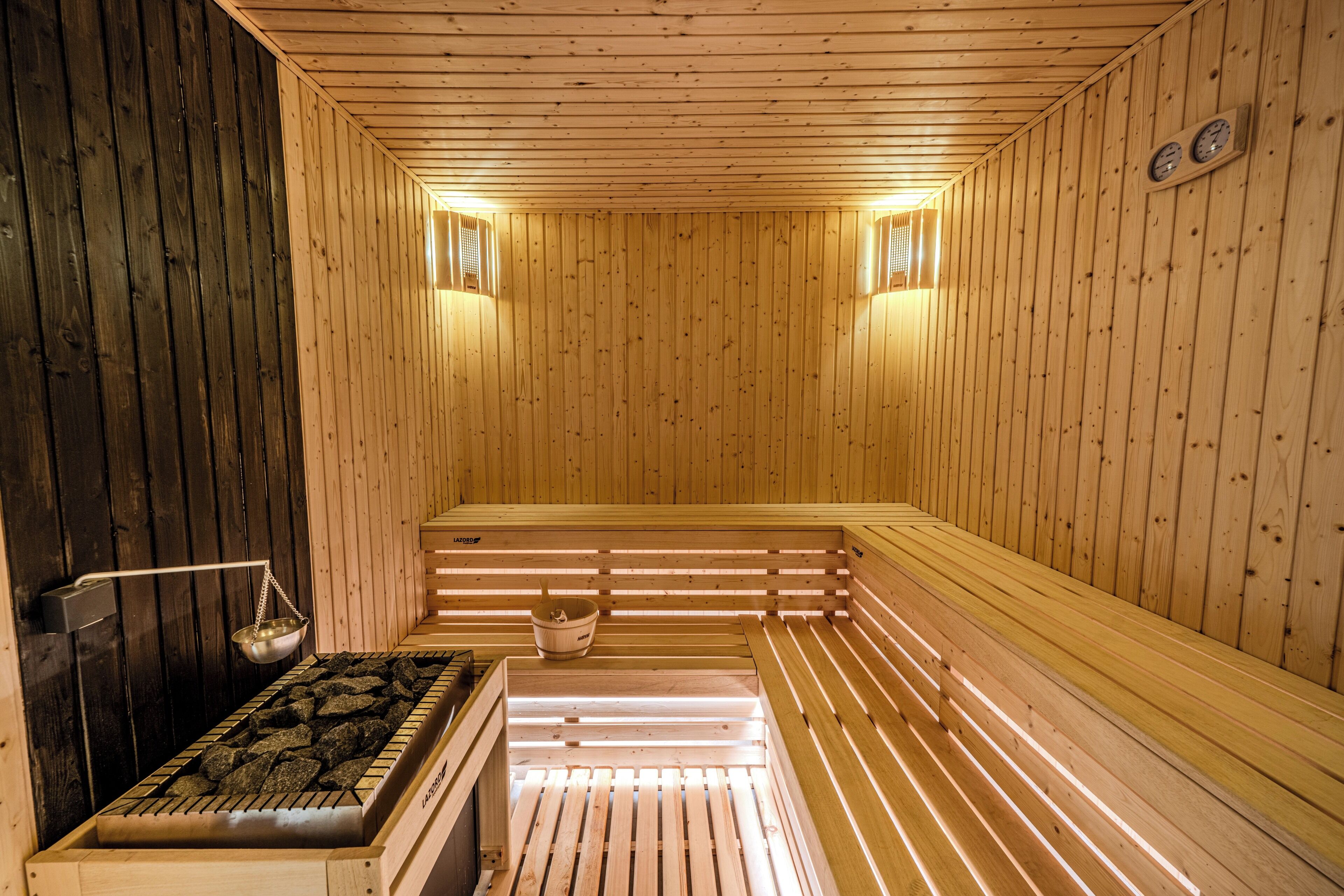 Eine Sauna mit Holzwänden, Bänken, einer Heizvorrichtung und zwei Wandleuchten.