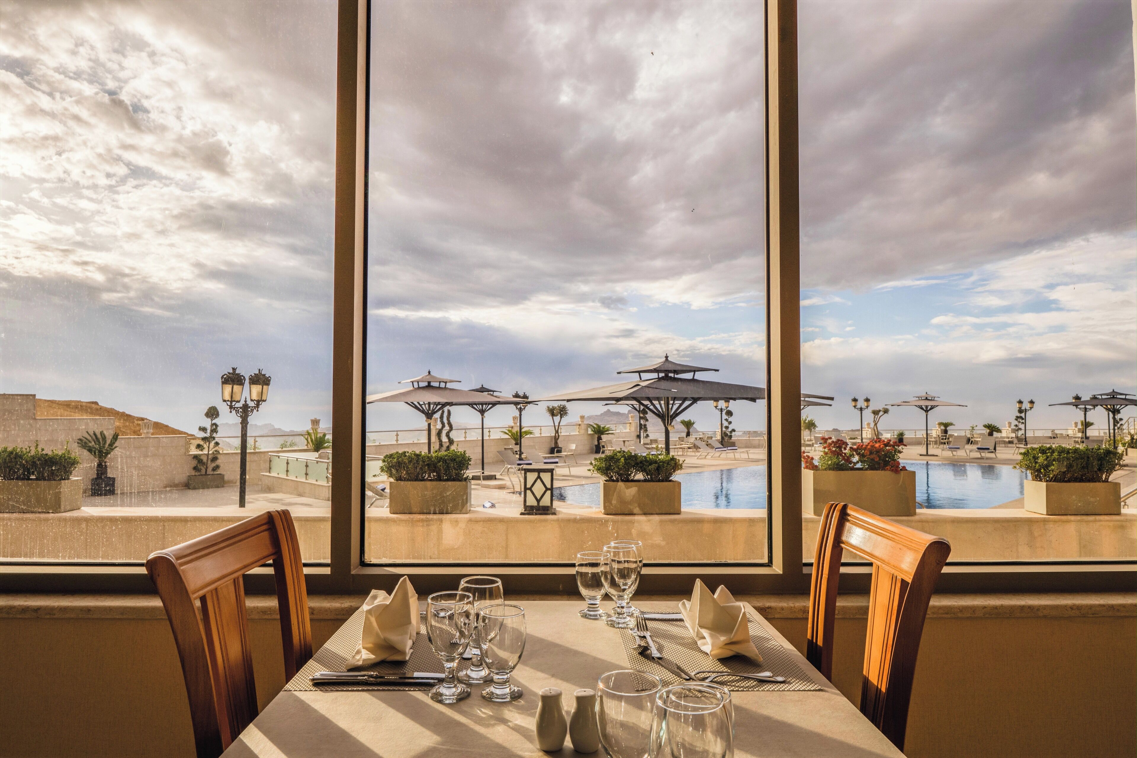 Mesa de comedor para cuatro con vista a una piscina y sombrillas.