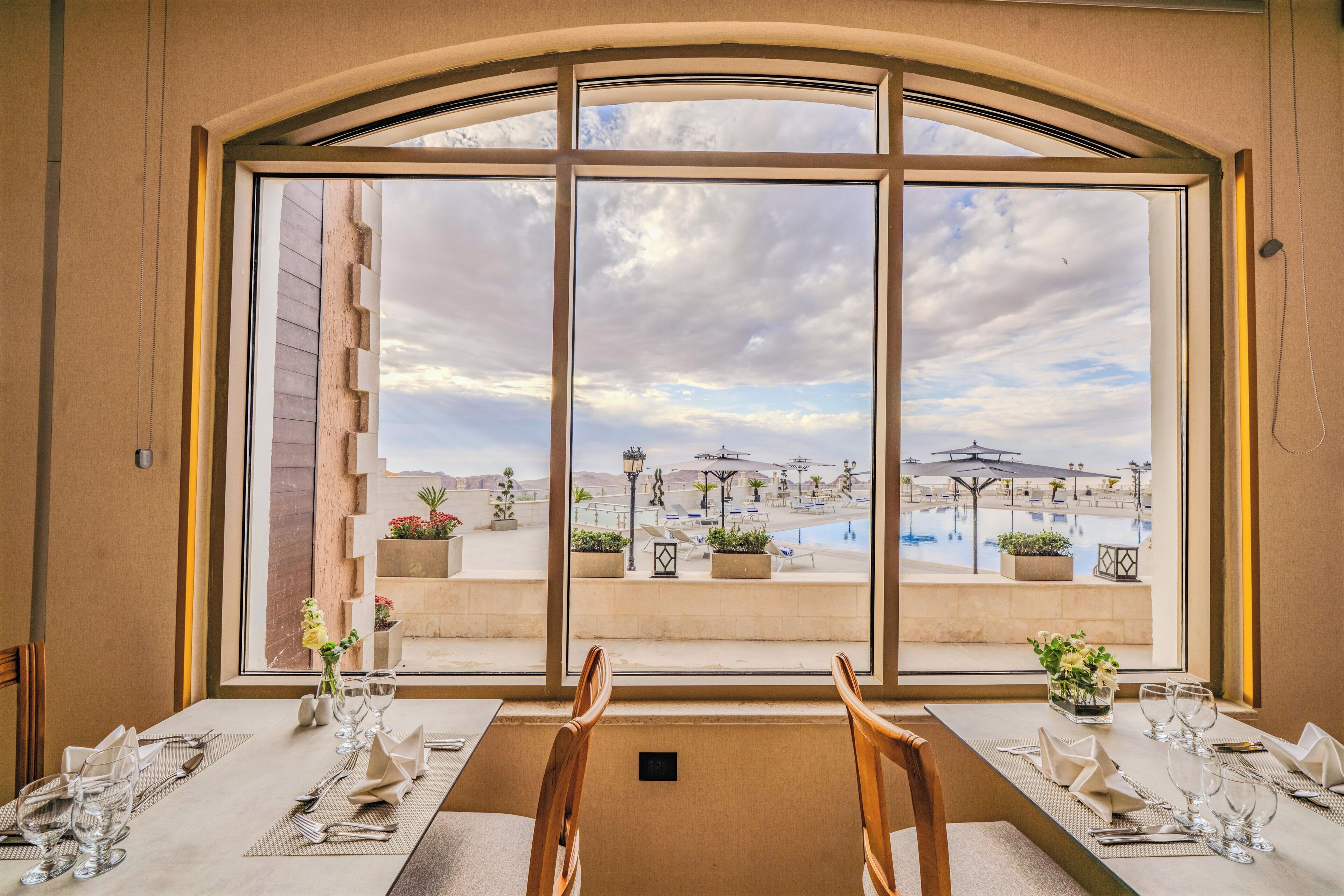 A dining area with a table set for two, large windows offering a view of a pool and outdoor seating area.