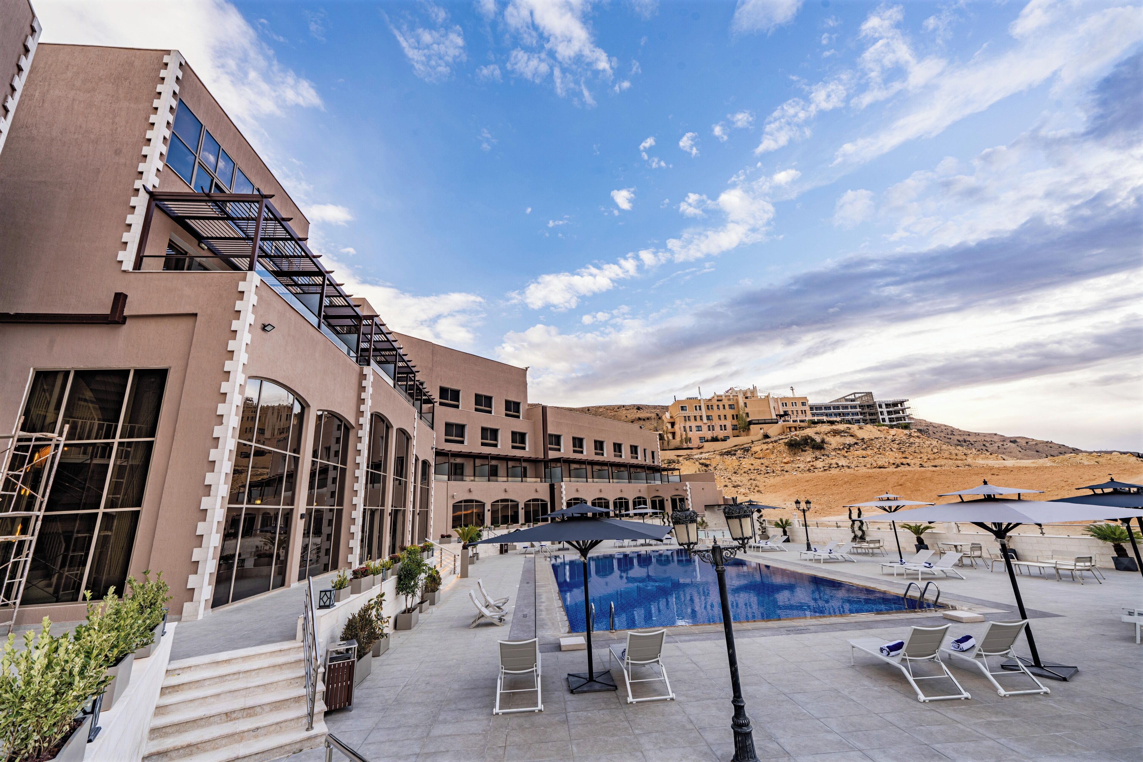 A hotel with a swimming pool, outdoor seating, and a view of a hill.