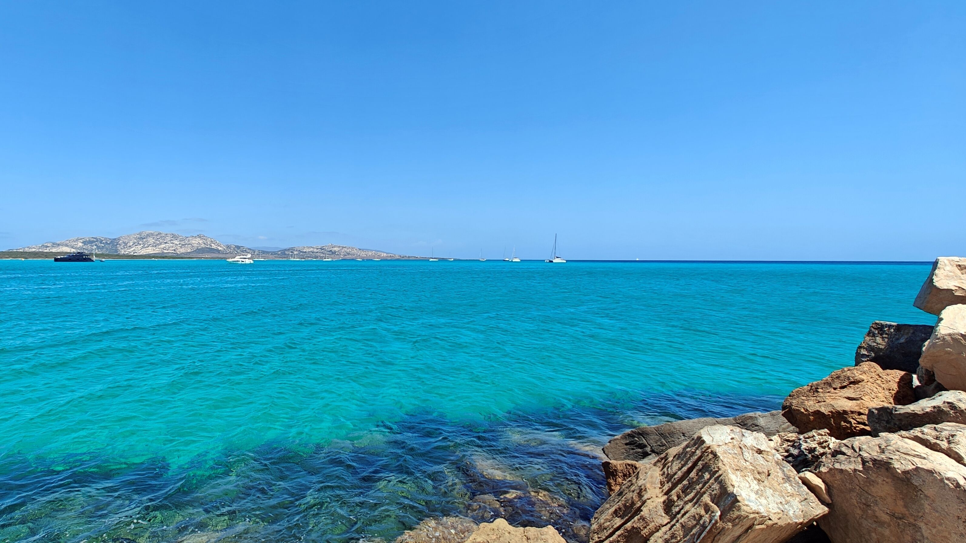 Helder turquoise water met rotsachtige oevers en boten in de verte.