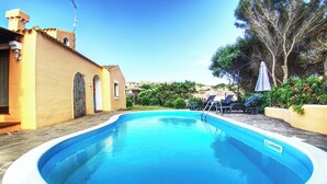 A swimming pool with a curved edge, surrounded by a low wall and a small building with arched windows. - Villa Blu with pool in Stintino – Sardinia (Punta de Su Turrione)