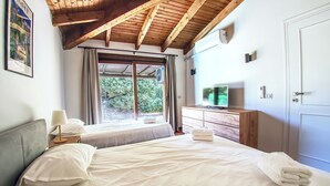 A bedroom with a bed, a nightstand, a dresser, a television, and a window with curtains. - Villa Blu with pool in Stintino – Sardinia (Punta de Su Turrione)