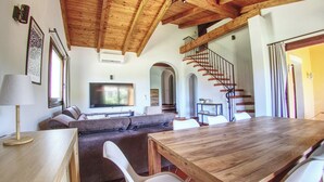 A spacious living area with a wooden dining table, a sofa, and a TV. - Villa Blu with pool in Stintino – Sardinia (Punta de Su Turrione)